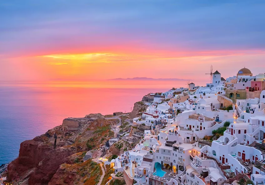 White-washed buildings of Oia, Santorini, perched on volcanic cliffs overlooking the sea during a vibrant sunset.