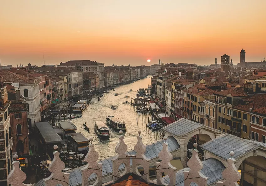 High-angle view of the Grand Canal in Venice at sunset, featuring historic buildings and boats on the water.
