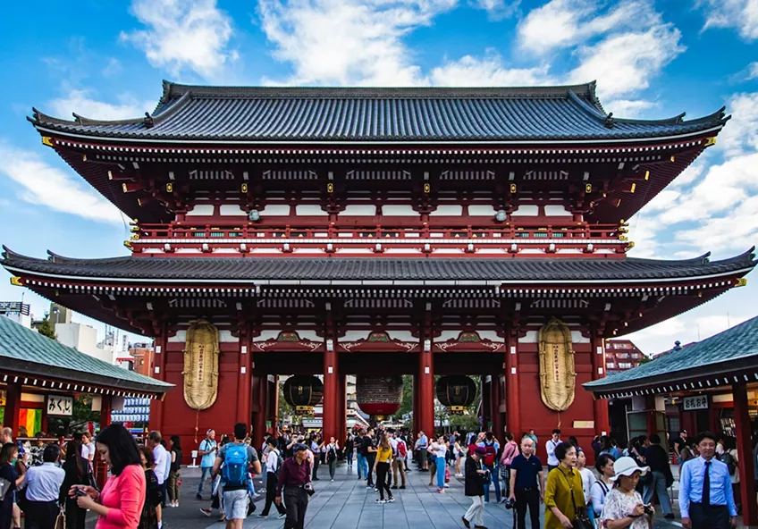 Large red and black Japanese temple gate (Senso-ji) with giant lanterns and crowds under a blue sky.