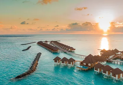 Crystal clear turquoise water gently lapping onto a white sand beach with lush palm trees under a bright sun.