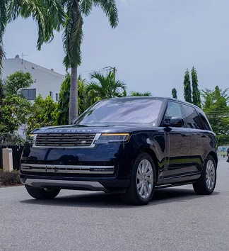 Dark navy blue Range Rover SUV parked on a paved driveway surrounded by tropical palm trees and white buildings.