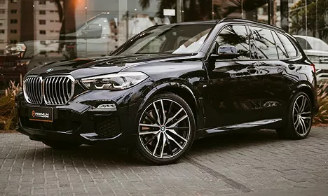 Gloss black BMW X5 SUV with large alloy wheels parked on a paved surface in an urban setting.