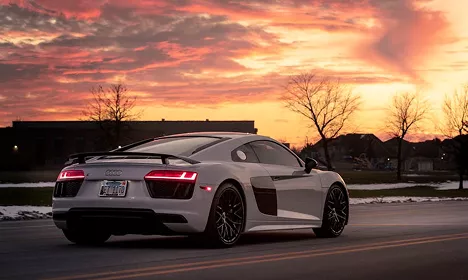 White Audi R8 coupe photographed from the rear on a road against a vivid pink and orange sunset sky.