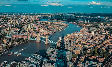 Aerial view of London showing Tower Bridge spanning the River Thames with the city skyline stretching into the distance.