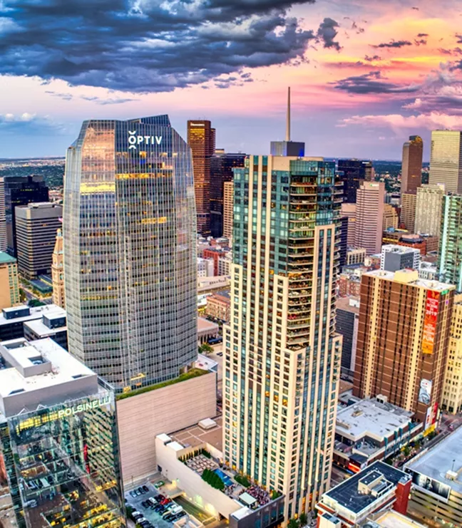 A vibrant sunset view of the Denver skyline, featuring the Optiv building and modern high-rises under a dramatic pink and purple sky.