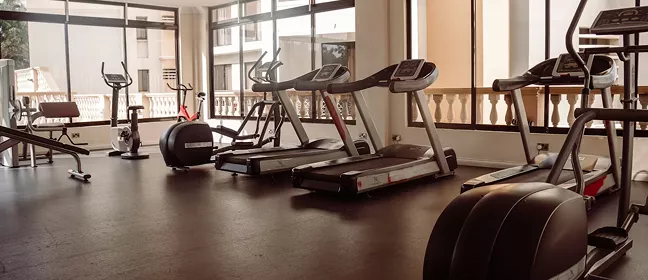 Hotel fitness centre with treadmills, an elliptical, and a stationary bike on dark rubber flooring beside large windows.