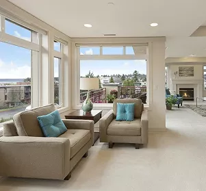 Bright lounge with beige sofas, teal cushions, floor-to-ceiling windows with city views, and a fireplace in the background.