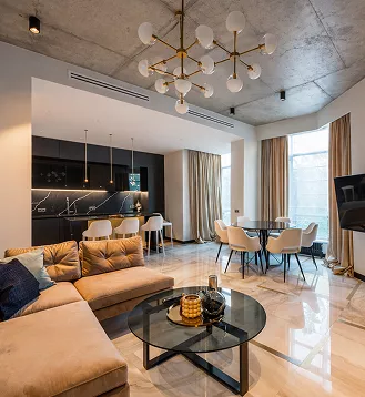 Modern open-plan apartment with a tan sectional sofa, round glass coffee table, and gold Sputnik chandelier.