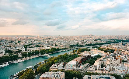 High-angle view of Paris featuring the Seine River winding through dense architecture, lush green trees, and historical stone buildings.